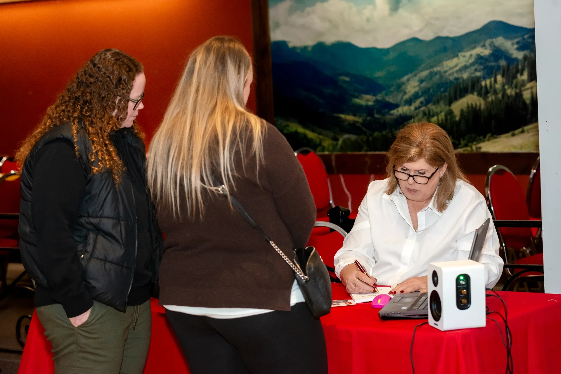 Janet signing a copy for two readers in front of the mountain mural